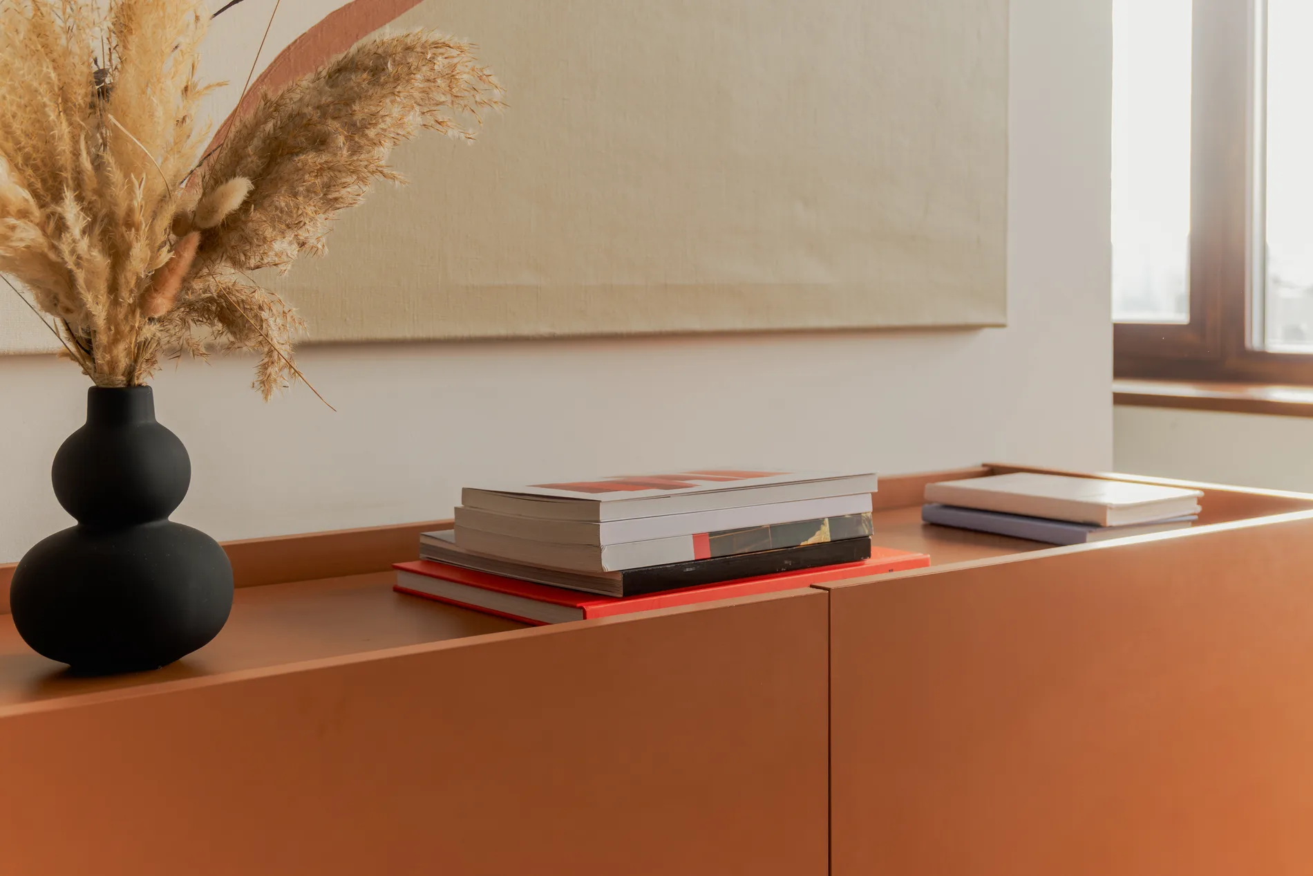 Terrakottafarbenes Sideboard mit Vase, Trockengräsern und Büchern als Sinnbild für W12 Living
